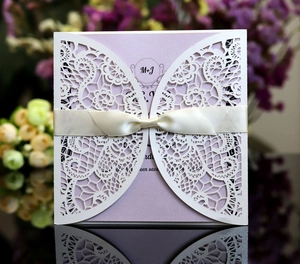 Detail of laser-cut wedding invitation with cream hollow floral cover and purple ribbon