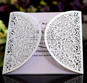 Close-up of laser-cut rose patterns on a white wedding invitation with a pink insert card