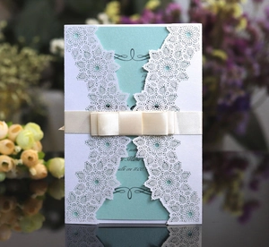 Elegant laser-cut lace wedding invitations with light blue insert and cream ribbon bow