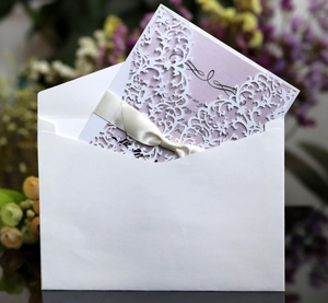 Close-up of laser cut white lace wedding invitation with lavender card and silk bow