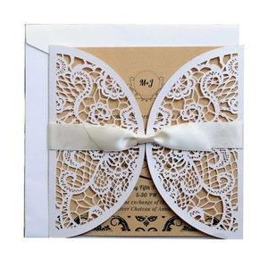 Laser cut white wedding invitation with lace patterns, satin ribbon, and kraft insert