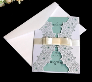 Detail of laser-cut wedding invitation with white floral shell and champagne satin bow