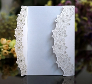 Detail of laser cut lace floral patterns on white pearlescent paper invitation card