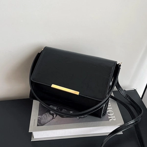 Classic black crossbody bag in glossy faux leather with gold buckle on a magazine