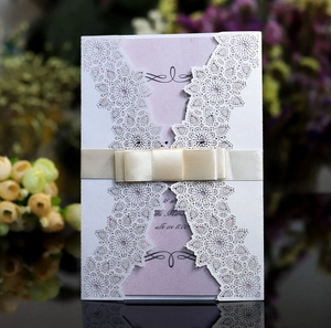 Close-up of laser-cut lace wedding invitation with a cream ribbon and delicate bow detail