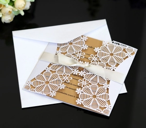 Close-up of laser-cut snowflake invitation with white silk ribbon and kraft paper insert