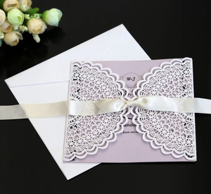 Detail of laser-cut white wedding invitation with lavender card and silk ribbon bow