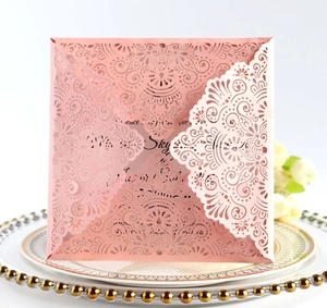 Detailed laser-cut lace wedding invitation with elegant pink floral patterns on dinner plate