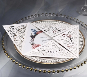 Close-up of laser-cut white wedding invitation with floral patterns and colored insert