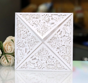 Close-up of laser-cut white wedding invitation featuring intricate floral rose patterns