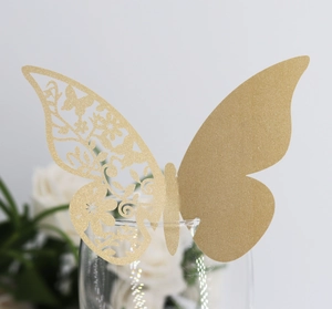 Detail of laser-cut gold butterfly place card on wine glass for wedding decor
