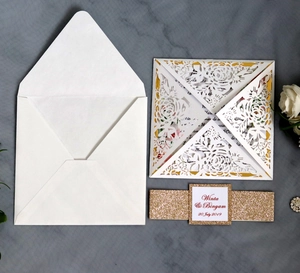 Close-up of laser cut ivory wedding invitation with glitter gold belly band and envelope