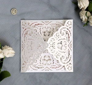 Elegant white laser cut wedding invitation with lace pattern on grey textured background