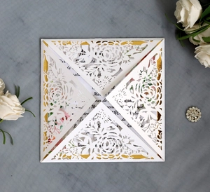 Close-up of laser-cut white wedding invitation with gold base and elegant rose accents