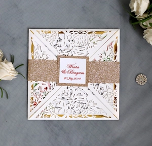 Detail of white laser-cut wedding invitation with gold glitter band and custom tag