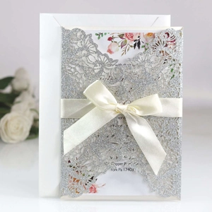 Detail of silver glitter laser cut wedding invitation with satin bow and floral insert
