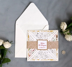 Macro shot of laser-cut floral wedding invitation with gold glitter belly band and envelope