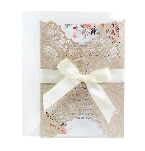Close-up of laser-cut rose gold glitter wedding invitation with satin bow and floral card