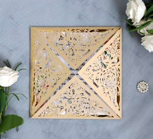 Detail view of laser-cut gold wedding invitation with floral patterns on fabric background