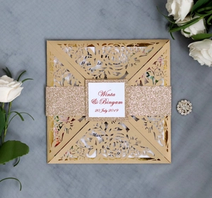 Detailed laser-cut gold wedding invitation featuring floral lace patterns and champagne glitter band