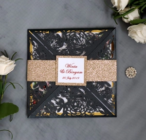 Detail of laser-cut wedding invitation with black floral pattern and gold glitter band