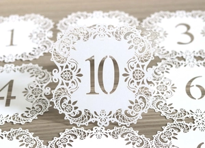 Detail of laser-cut white wedding table number cards with elegant lace hollow patterns