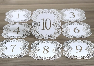 Detailed laser-cut wedding table number card with white lace design on wooden background