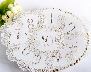 Close-up of white laser-cut wedding table cards with hollow floral patterns and numbers
