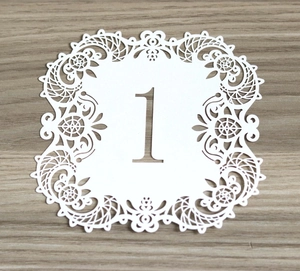 Detailed laser-cut white hollow wedding table number card with number one on wood surface