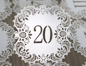 Detailed laser-cut wedding table number card showing white lace floral patterns and digit 20