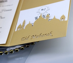 Macro detail of laser-cut Eid Mubarak invitation card with champagne gold pearlescent finish