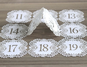 Macro view of white laser-cut wedding table cards with hollow floral lace and number details
