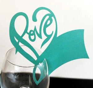 Détail d'un marque-place cœur bleu tiffany avec découpe Love sur un verre à vin