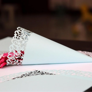 Laser-cut light blue paper confetti cone with intricate hollow flower pattern for weddings