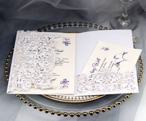 Detail of laser-cut floral wedding invitation with purple illustrations on a glass tray