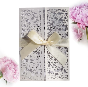 Detailed close-up of a white laser-cut floral wedding invitation with cream satin ribbon