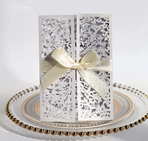Detailed laser-cut floral pattern and silk ribbon bow on a white wedding invitation