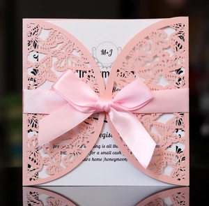 Macro detail of laser cut butterfly wedding invitation with pink ribbon bow and lace shell