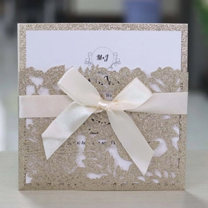 Detail of laser-cut floral invitation with champagne gold glitter and cream satin ribbon