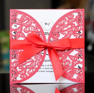 Detail of red laser-cut butterfly invitation with satin ribbon bow and elegant script