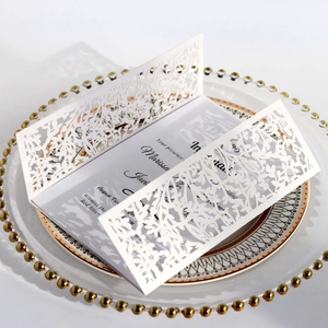 Elegant white laser-cut floral wedding invitation card set on a white ceramic plate