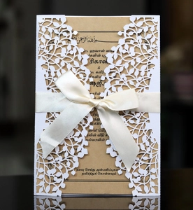 Close-up of laser-cut leafy design invitation with kraft paper and white ribbon bow