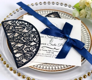 Detail of laser-cut butterfly invitation cover with navy glitter finish and satin ribbon