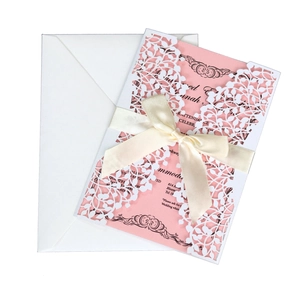 Macro shot of laser-cut floral patterns on pink invitation card with white satin bow detail