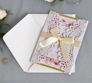 Detail view of laser-cut wedding invitation with cream silk bow and floral insert card