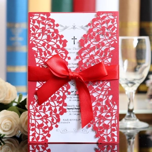 Detail of red laser-cut wedding invitation with satin ribbon and elegant floral hollow design