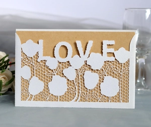 Detail of laser cut white lace invitation with LOVE lettering and kraft paper insert