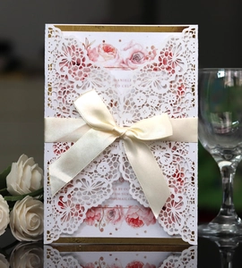 Elegant white laser-cut lace wedding invitation with ribbon bow and floral inner card