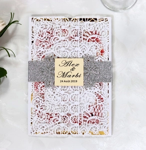Macro detail of laser-cut lace wedding invitation with silver glitter belt and floral liner