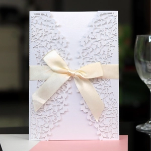 Elegant laser-cut leaf pattern white wedding invitation with a beige satin bow decoration